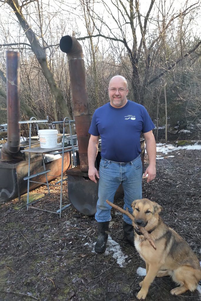 A middle aged bald man with dog by boiler outside